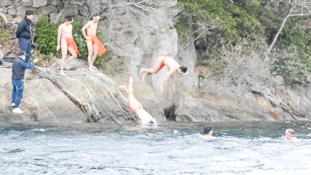 権現島の鳥居の横の岩から海へ飛び込む若者